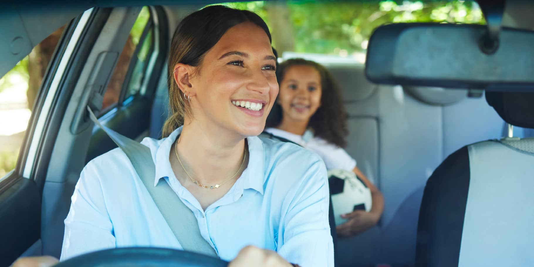 A smiling woman looking through her vehicle rear view mirror at her young daughter.