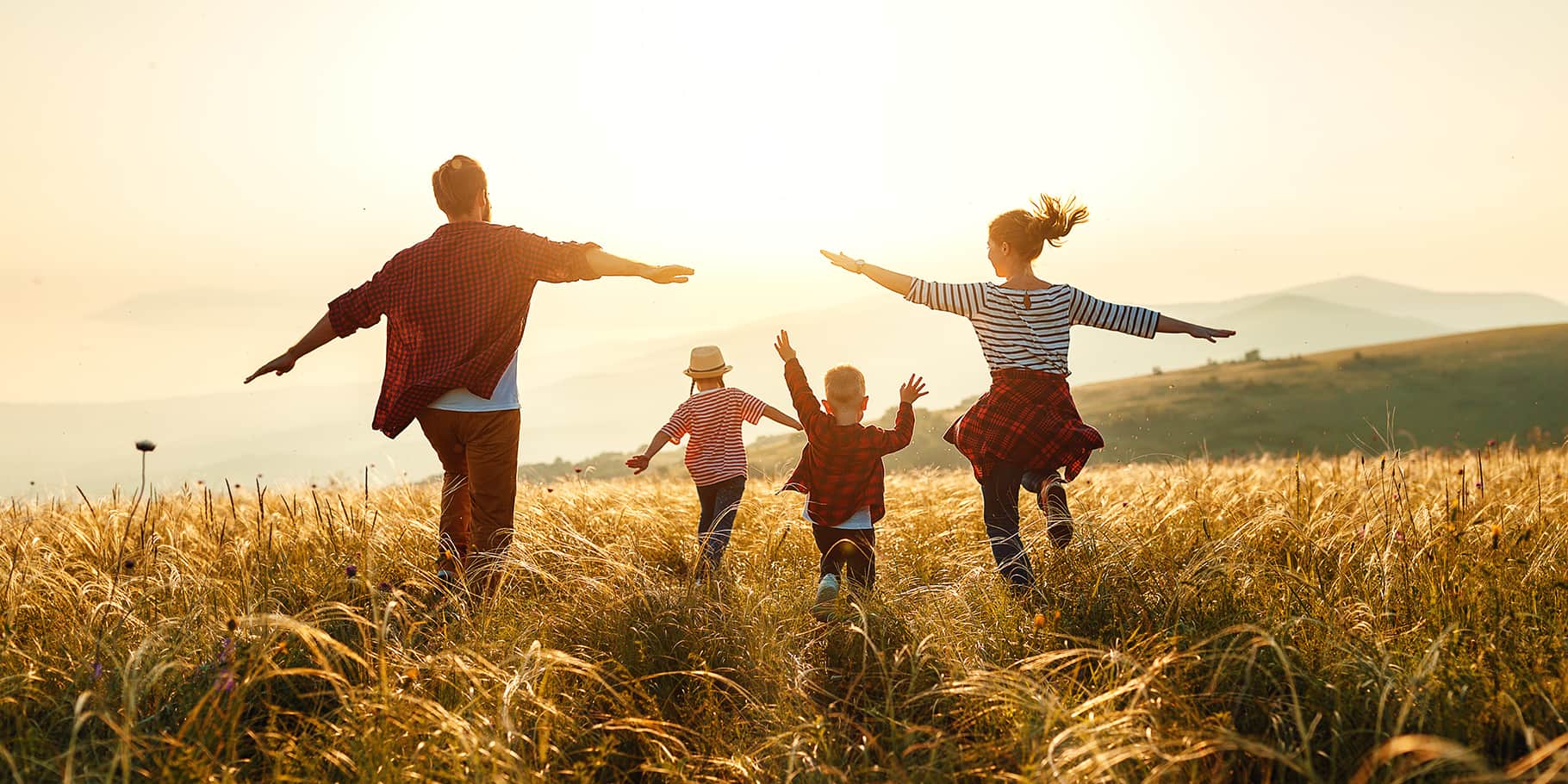 A family of four running through wheat fields.